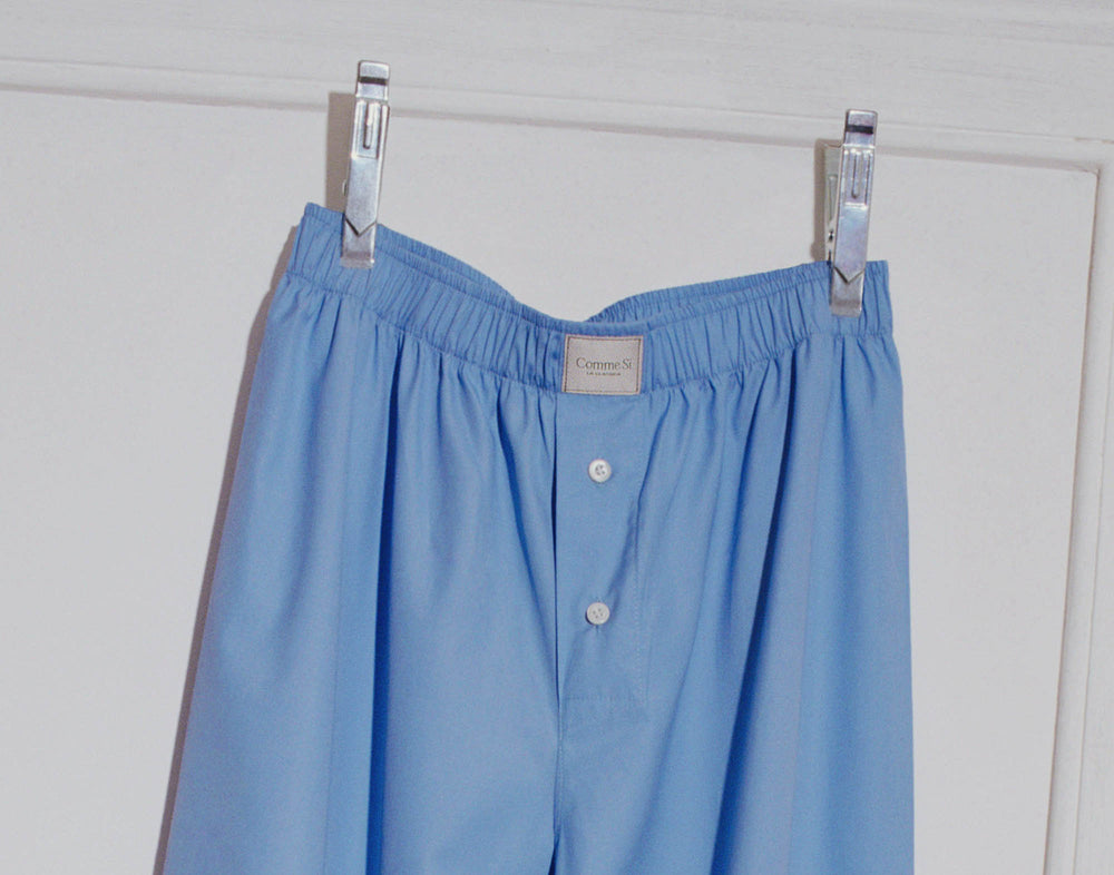 la boxer alta cotton poplin in grecian blue. long blue cotton boxer pants hang from two silver clips in front of a white background. the photo is taken with flash