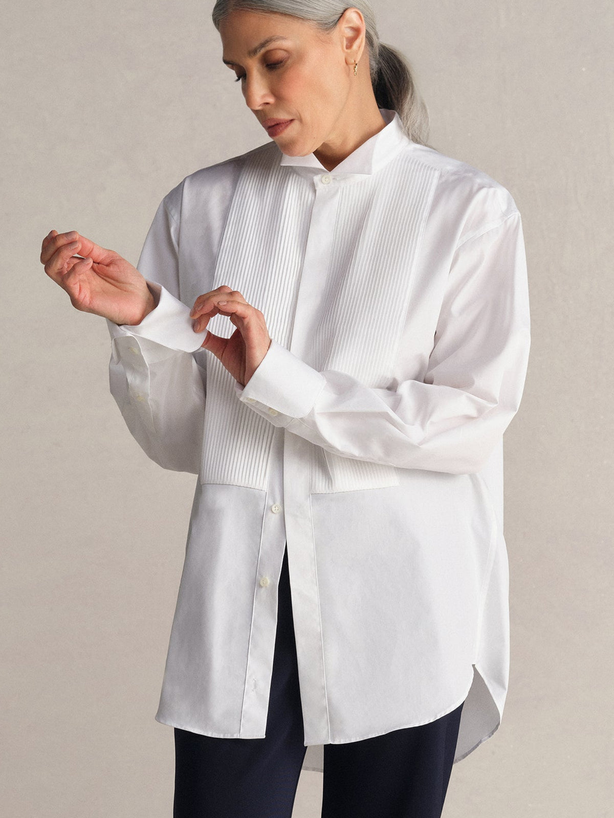 A model wearing a Comme Si white long-sleeve button-up shirt and midnight bias pant, standing against a neutral beige studio background.
