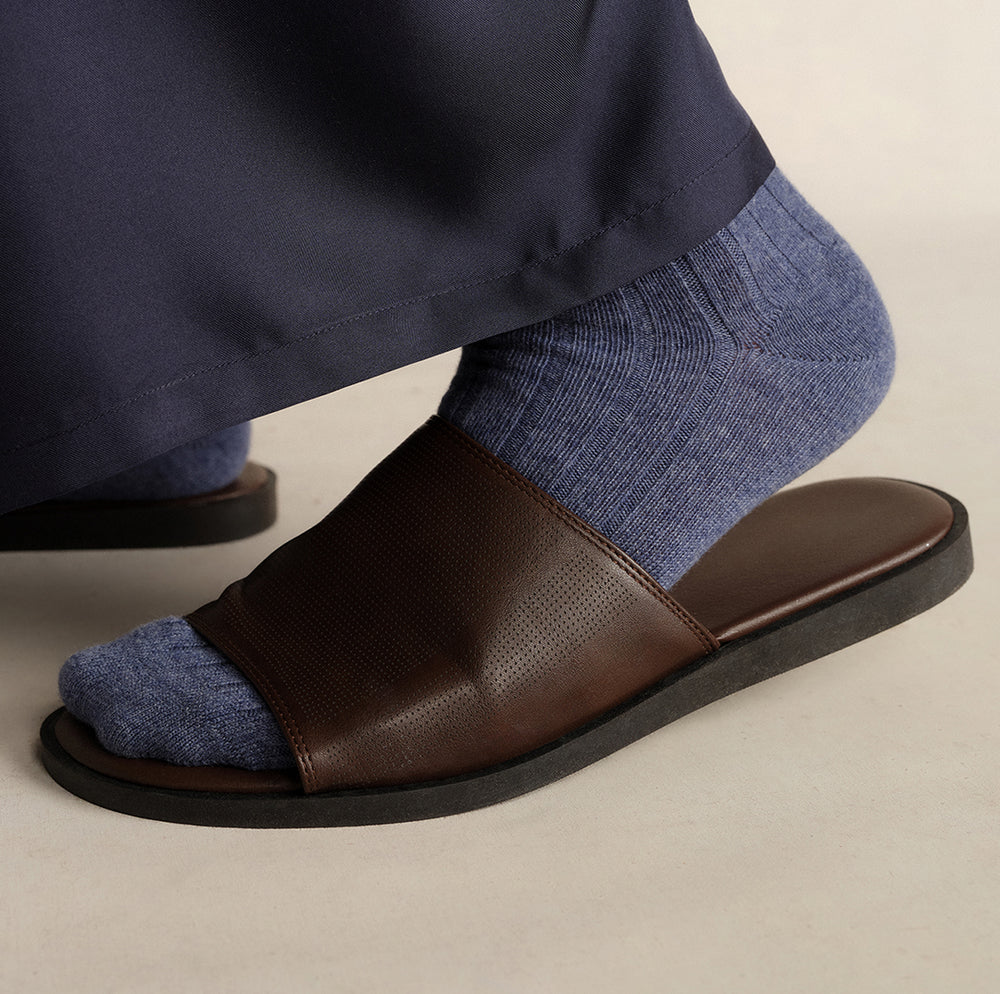 Close-up of blue ribbed cashmere socks worn with brown leather slide sandals and navy silk twill pants by Comme Si.