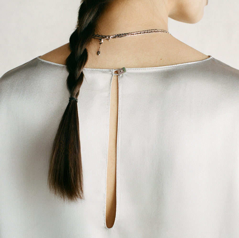 Back view of a model wearing a Comme Si silver bell sleeve top with a long keyhole opening and button closure.