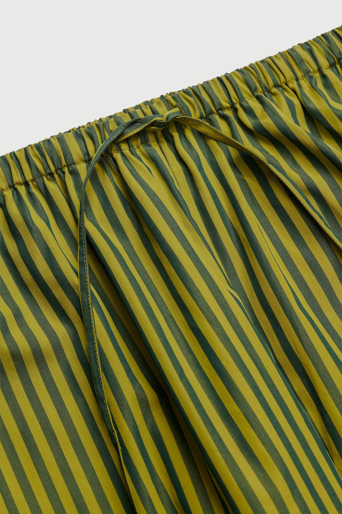 Close-up of a striped garment, likely shorts or pajama pants, featuring vertical stripes in olive green and mustard yellow with a matching drawstring waist.