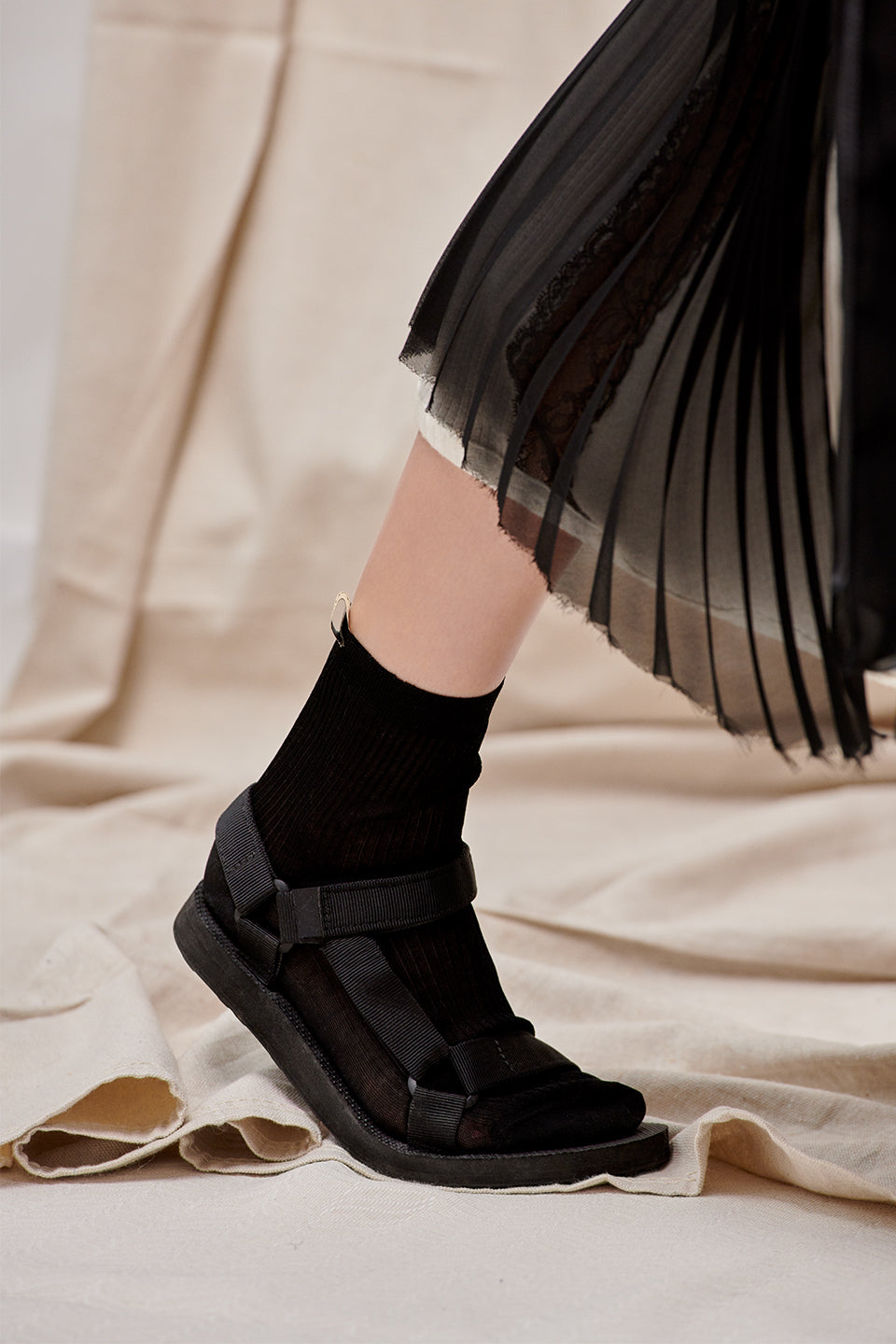 The Agnelli Sock in black with black velcro sandals and a sheer black pleated skirt