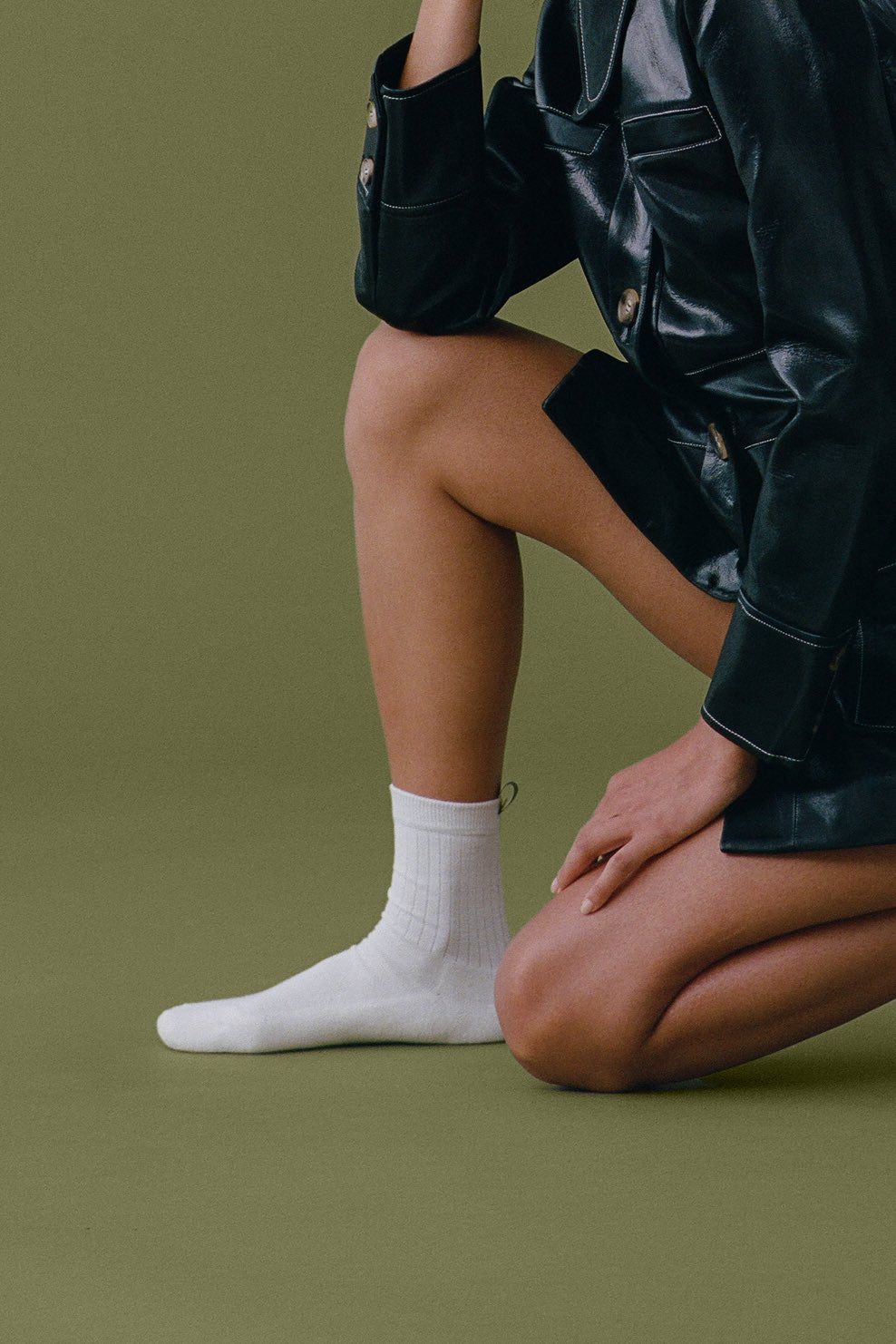 Michelle wears The Everyday Sock in Off White with a black leather jacket on an olive green backdrop.